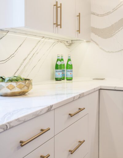 A white kitchen with marble counter tops and a bottle of water.