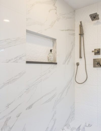 A white shower with marble tile and a shower head.