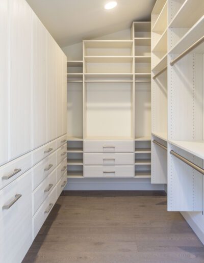 A walk in closet with white cabinets and drawers.