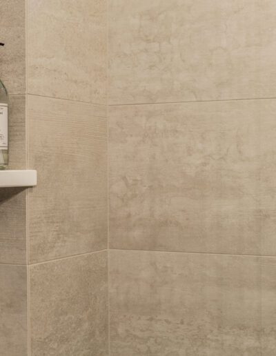 A beige tiled shower with a bottle of water.