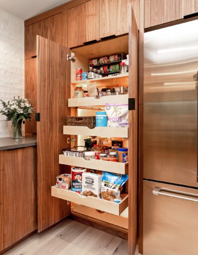 A kitchen with a stainless steel refrigerator and a pull out pantry.