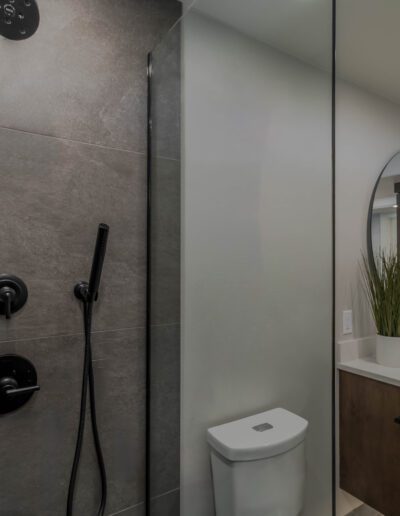 Modern bathroom interior with gray tiles, a glass shower enclosure, a white sink, and built-in wall shelves.