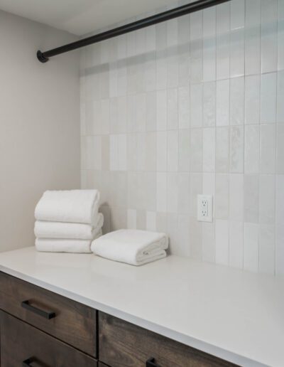 A modern bathroom counter with stacked white towels, dark cabinetry, and a light tiled wall.