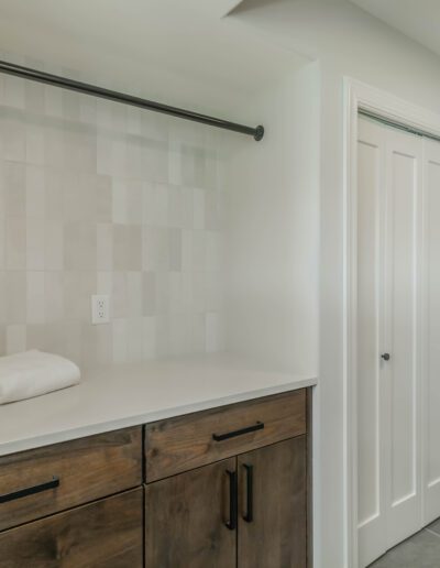 Modern bathroom interior with a wooden vanity cabinet, white countertop, stacked white towels, and a closed white door. light neutral tones with tiled wall.