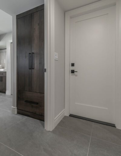 Interior corner showing a dark wood door on the left and a white door on the right, meeting at white trim on a gray tiled floor.